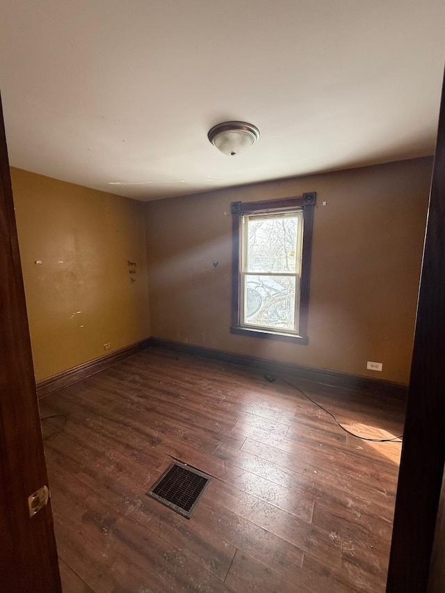 empty room featuring dark wood-style flooring, visible vents, and baseboards