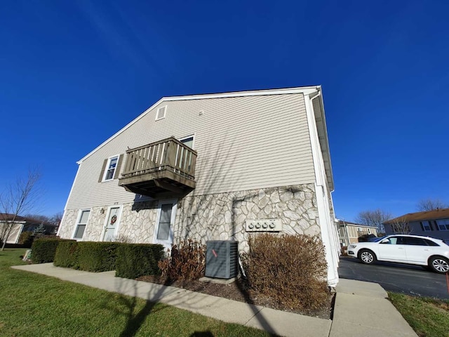 view of side of property featuring central air condition unit, stone siding, and a balcony