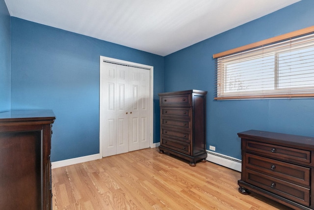 bedroom with baseboards, baseboard heating, a closet, and light wood-style floors