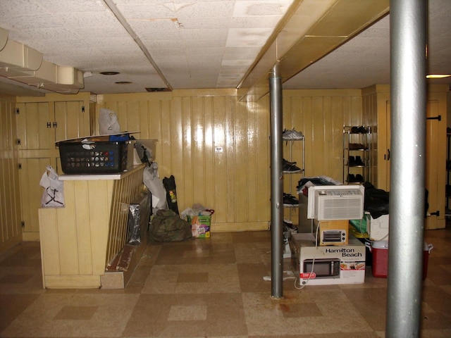 finished below grade area featuring wooden walls, an AC wall unit, and tile patterned floors