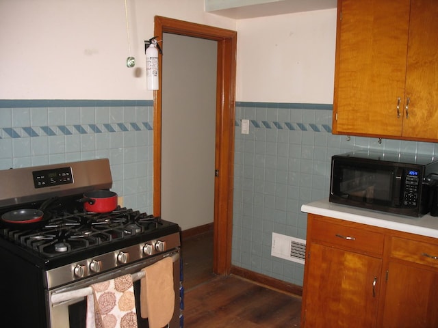 kitchen featuring brown cabinetry, black microwave, light countertops, and gas range