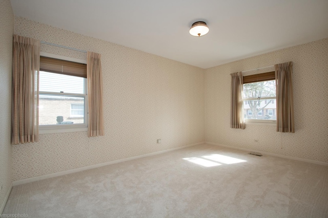 carpeted spare room featuring visible vents, baseboards, and wallpapered walls