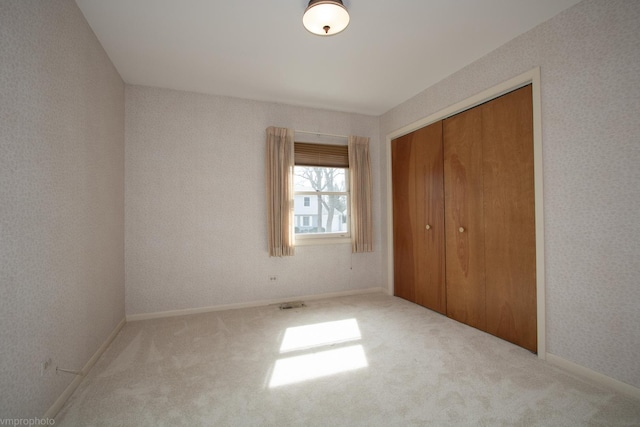 unfurnished bedroom with visible vents, wallpapered walls, baseboards, carpet, and a closet