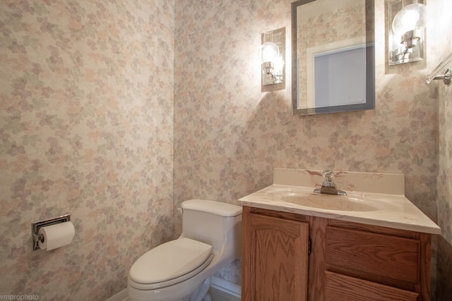 bathroom featuring toilet, wallpapered walls, and vanity