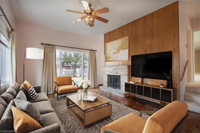 living room featuring stairs, wooden walls, ceiling fan, and a fireplace