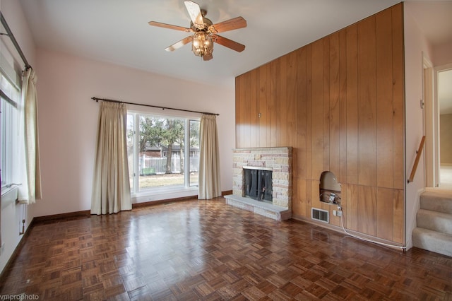 unfurnished living room featuring visible vents, a stone fireplace, wood walls, and stairs