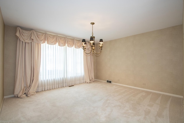 carpeted spare room featuring baseboards, visible vents, and a chandelier