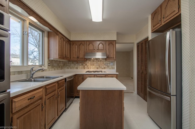 kitchen with under cabinet range hood, a sink, a center island, stainless steel appliances, and wallpapered walls