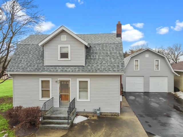 colonial inspired home featuring a garage, a shingled roof, a gambrel roof, driveway, and a chimney