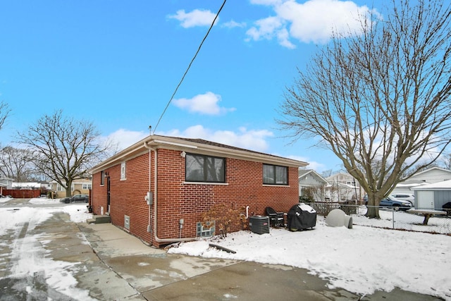 view of snowy exterior with brick siding, fence, and central AC unit