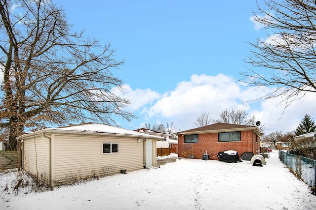 snow covered back of property featuring a detached garage, fence, and brick siding