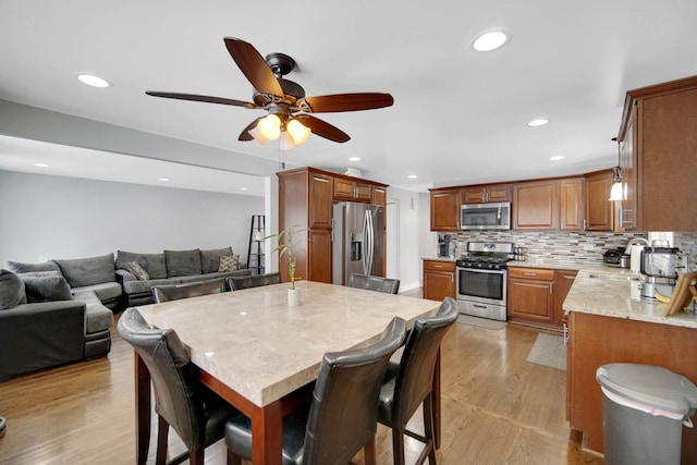 kitchen with brown cabinetry, light wood-style flooring, open floor plan, stainless steel appliances, and backsplash