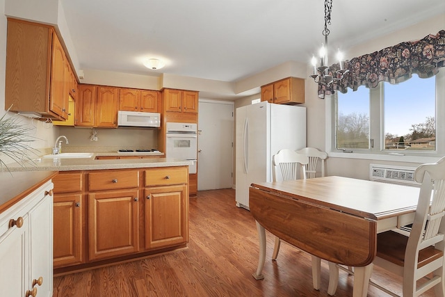 kitchen with white appliances, brown cabinetry, light wood-style flooring, decorative light fixtures, and a sink