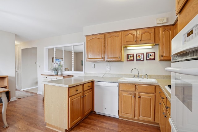 kitchen featuring a peninsula, white appliances, dark wood finished floors, and a sink