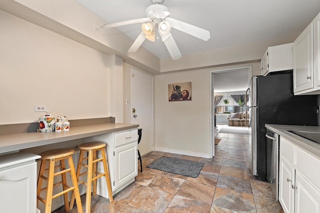 kitchen featuring ceiling fan, a breakfast bar, white cabinets, light countertops, and stone finish floor