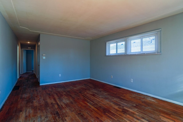 empty room featuring visible vents, baseboards, and dark wood-style flooring