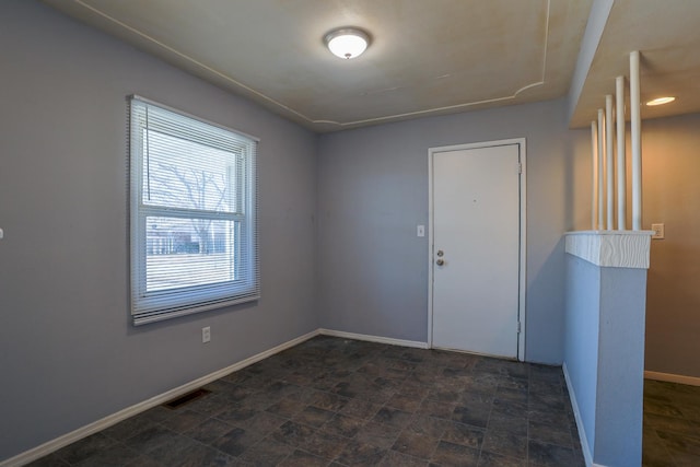 empty room with stone finish flooring, visible vents, and baseboards