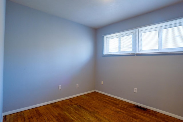 empty room with wood finished floors, visible vents, and baseboards