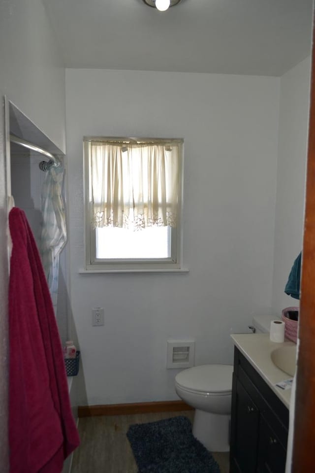 bathroom featuring toilet, wood finished floors, vanity, baseboards, and a shower