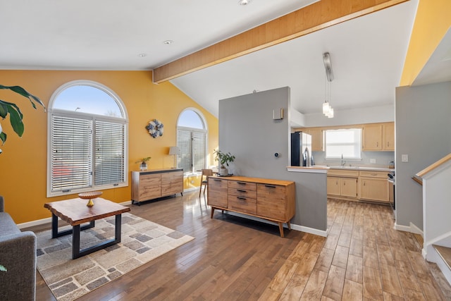 living area featuring light wood-type flooring, baseboards, and vaulted ceiling with beams