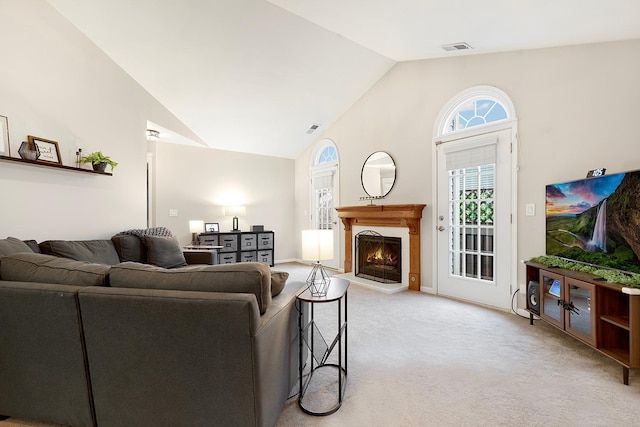 living area with a warm lit fireplace, high vaulted ceiling, visible vents, and light colored carpet