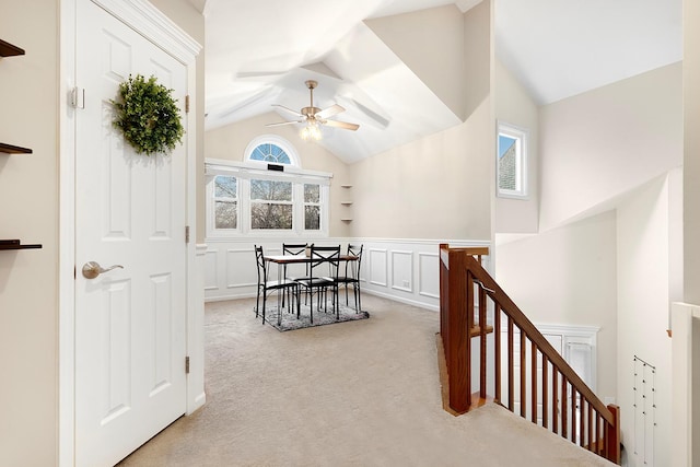 hallway featuring a wainscoted wall, carpet, vaulted ceiling, an upstairs landing, and a decorative wall