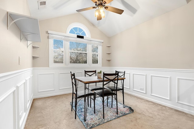 dining room with lofted ceiling, a wainscoted wall, visible vents, and light colored carpet