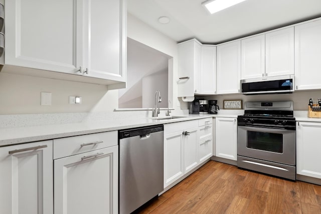 kitchen with appliances with stainless steel finishes, white cabinets, a sink, and light wood finished floors