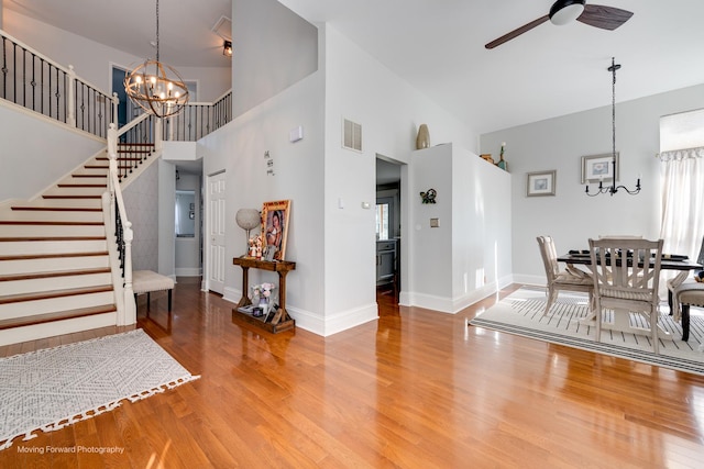 entrance foyer with visible vents, stairway, a towering ceiling, wood finished floors, and ceiling fan with notable chandelier