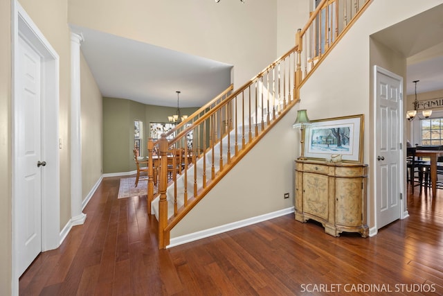 stairs featuring baseboards, a notable chandelier, a towering ceiling, and hardwood / wood-style flooring