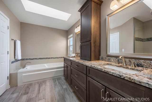 full bath featuring a bath, wood finished floors, a skylight, and a sink