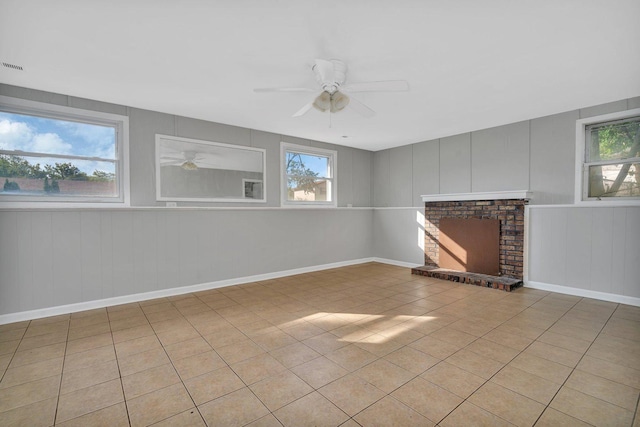 unfurnished living room with a healthy amount of sunlight, a brick fireplace, ceiling fan, and light tile patterned floors