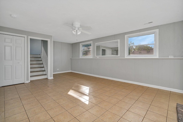 empty room with light tile patterned floors, visible vents, baseboards, a ceiling fan, and stairway