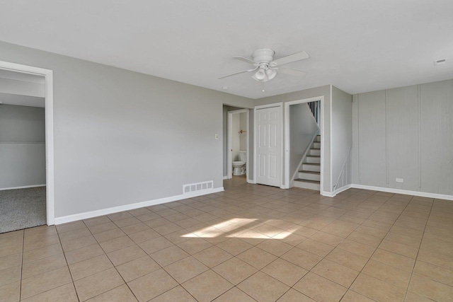 unfurnished room featuring light tile patterned floors, visible vents, baseboards, a ceiling fan, and stairway