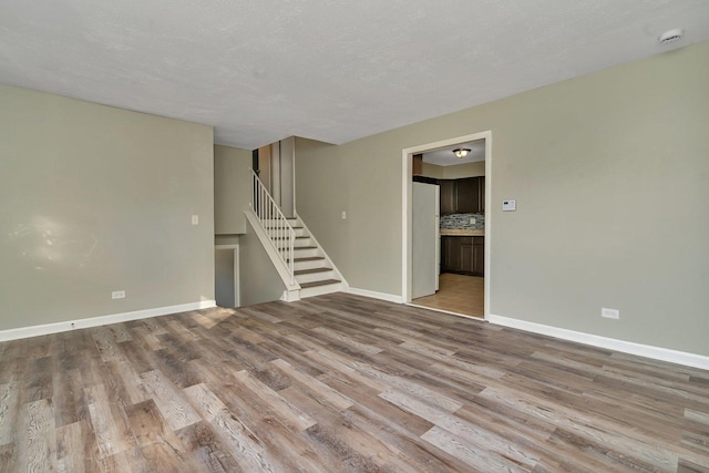 empty room with light wood-style floors, baseboards, and stairs