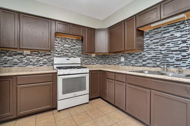 kitchen with a sink, white gas stove, light countertops, and decorative backsplash