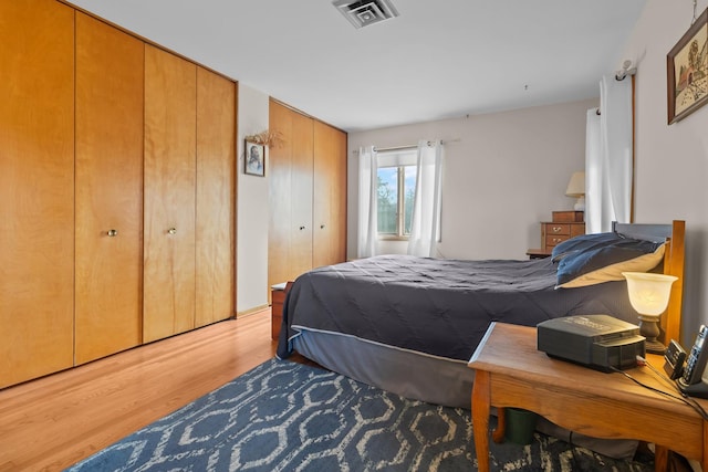 bedroom with light wood-style flooring, two closets, and visible vents