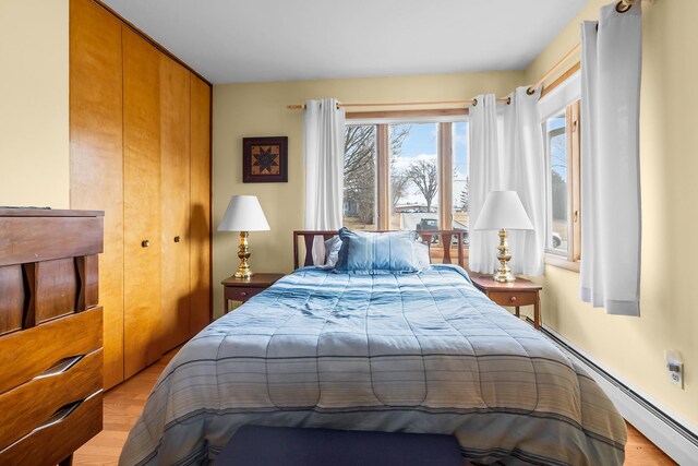 bedroom with light wood finished floors, a closet, and baseboard heating