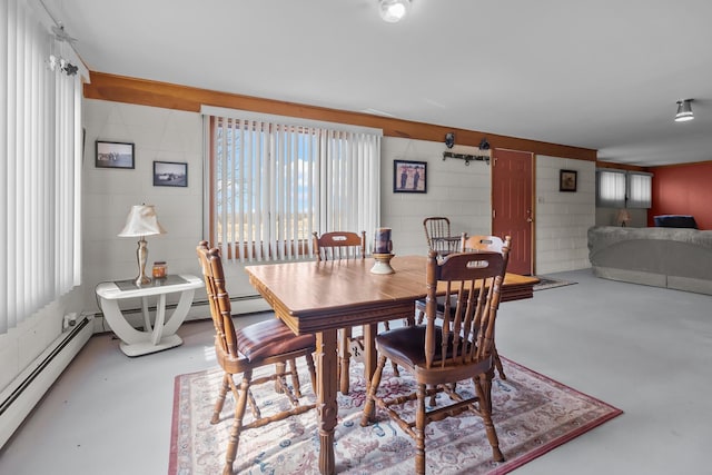 dining area featuring finished concrete flooring, a baseboard heating unit, and concrete block wall