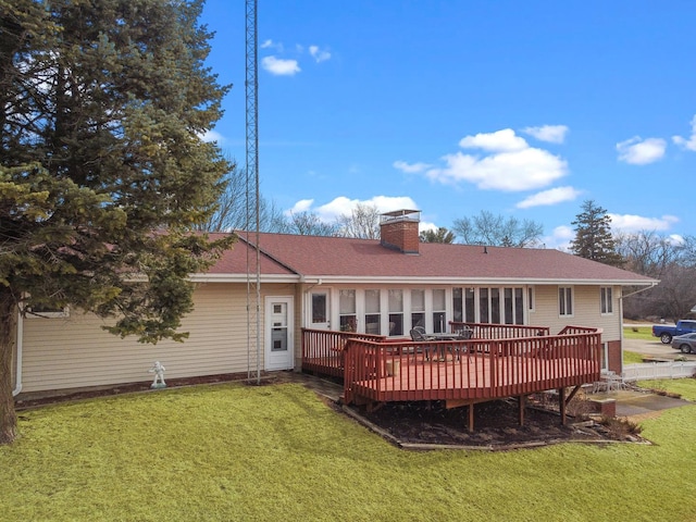 back of property with a chimney, a deck, a lawn, and roof with shingles