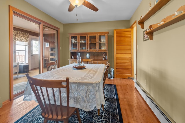 dining room with a baseboard heating unit, light wood-style flooring, and a ceiling fan