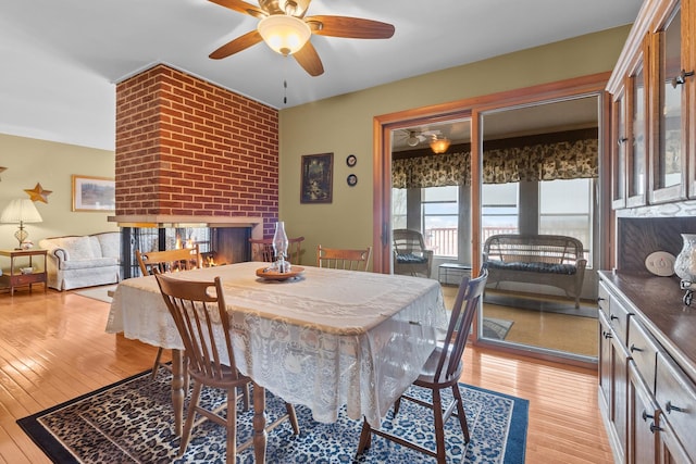 dining space with light wood finished floors, a fireplace, and a ceiling fan