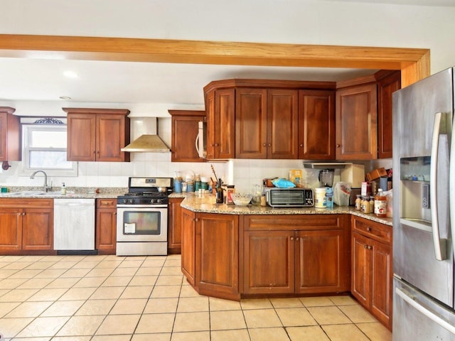 kitchen featuring light tile patterned floors, stainless steel appliances, a sink, wall chimney range hood, and light stone countertops