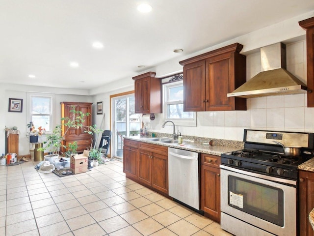 kitchen with wall chimney exhaust hood, a sink, light stone countertops, stainless steel appliances, and backsplash