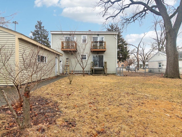 rear view of property with entry steps, a lawn, fence, and a balcony