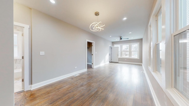 unfurnished living room with ceiling fan with notable chandelier, baseboards, wood finished floors, and recessed lighting