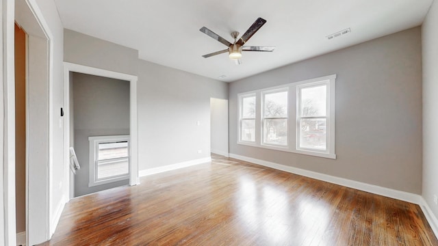 empty room with a ceiling fan, visible vents, plenty of natural light, and wood finished floors