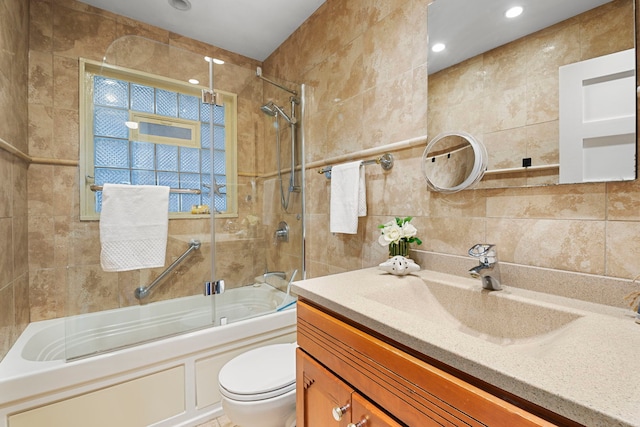 bathroom featuring toilet, combined bath / shower with glass door, tile walls, and vanity