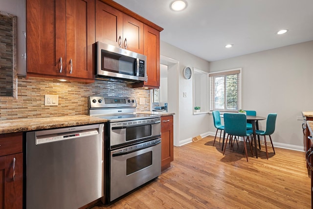 kitchen with recessed lighting, backsplash, appliances with stainless steel finishes, light wood-style floors, and light stone countertops