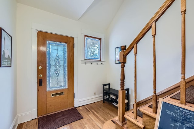 foyer featuring lofted ceiling, light wood finished floors, stairs, and baseboards